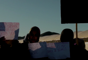Six women in a desert landscape hold up protest signs